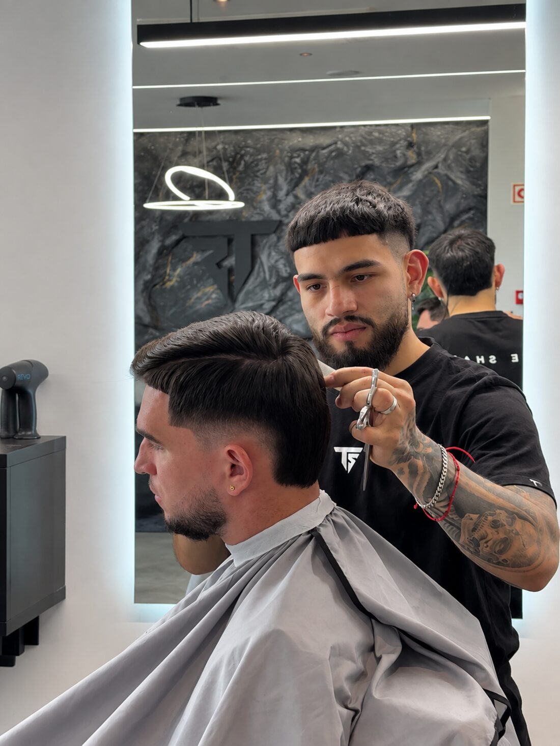 Barbeiro a trabalhar com tesoura, refletido no espelho da True Shape